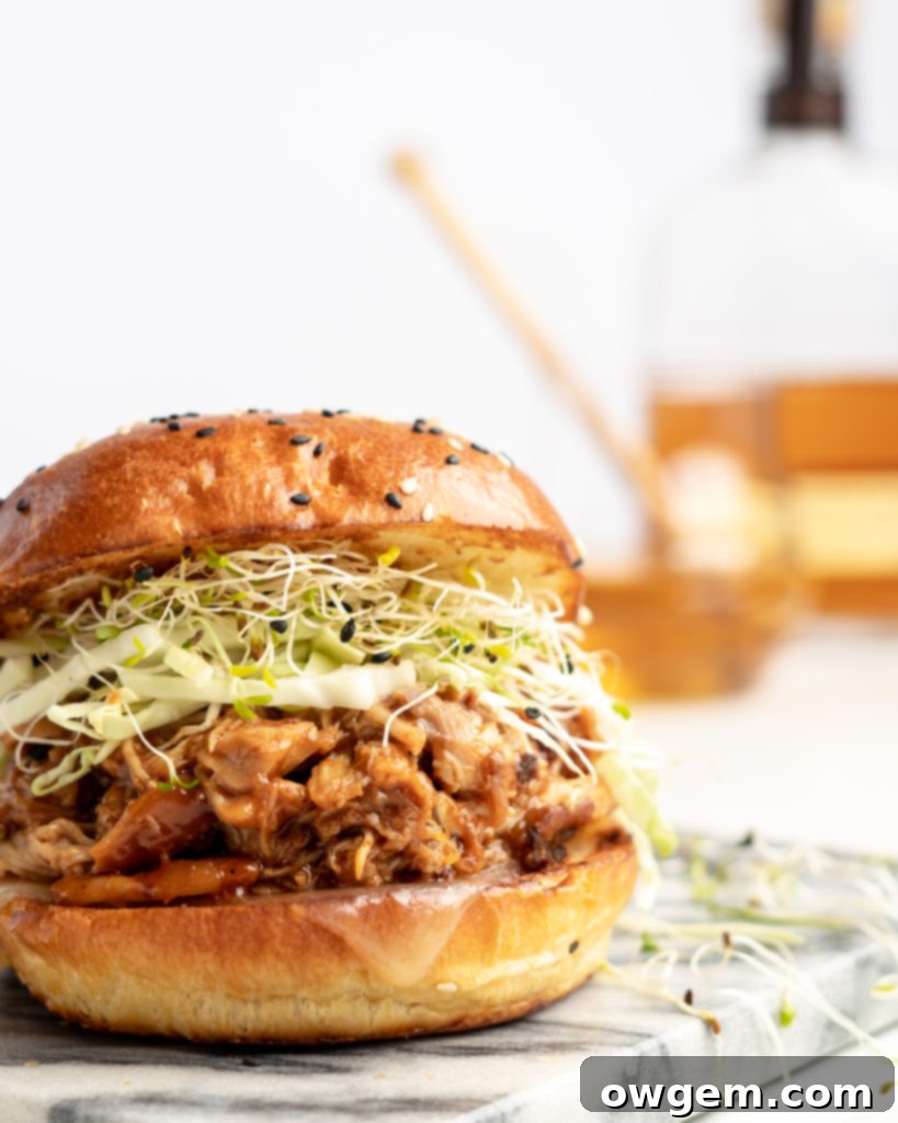 Close-up of a Slow Cooker BBQ Pulled Chicken Sandwich on a toasted bun with sharp white cheddar.