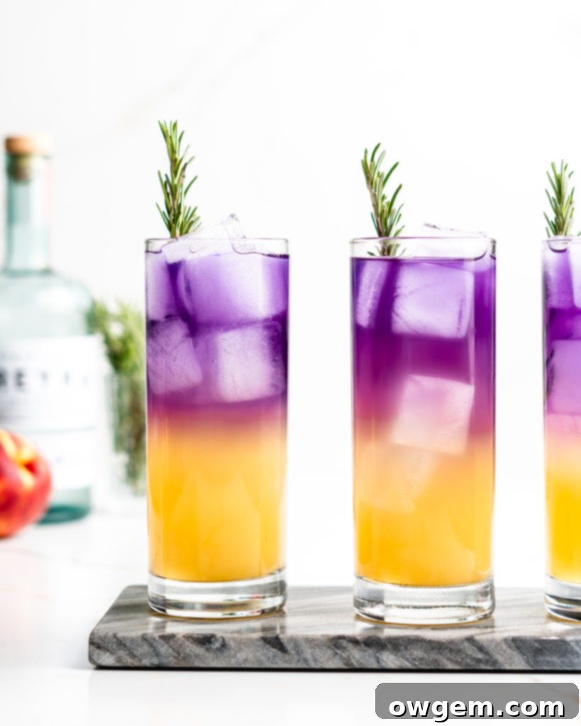 A highball glass filled with ice, vodka, sake, peach syrup, and soda water, with a separate shot glass holding deep blue butterfly pea flower tea and yuzu juice before mixing. Garnished with rosemary.