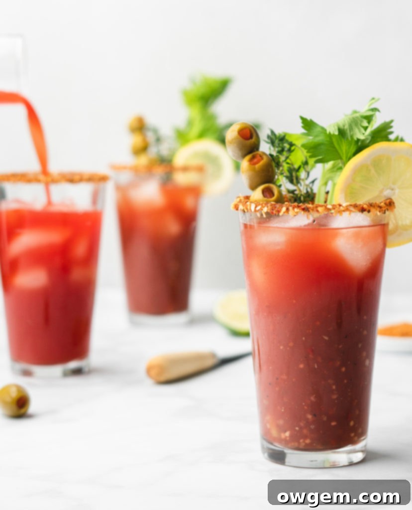 A close-up of a Caesar cocktail with a custom spiced rim, garnished with a lime wedge and a vibrant red pepper.