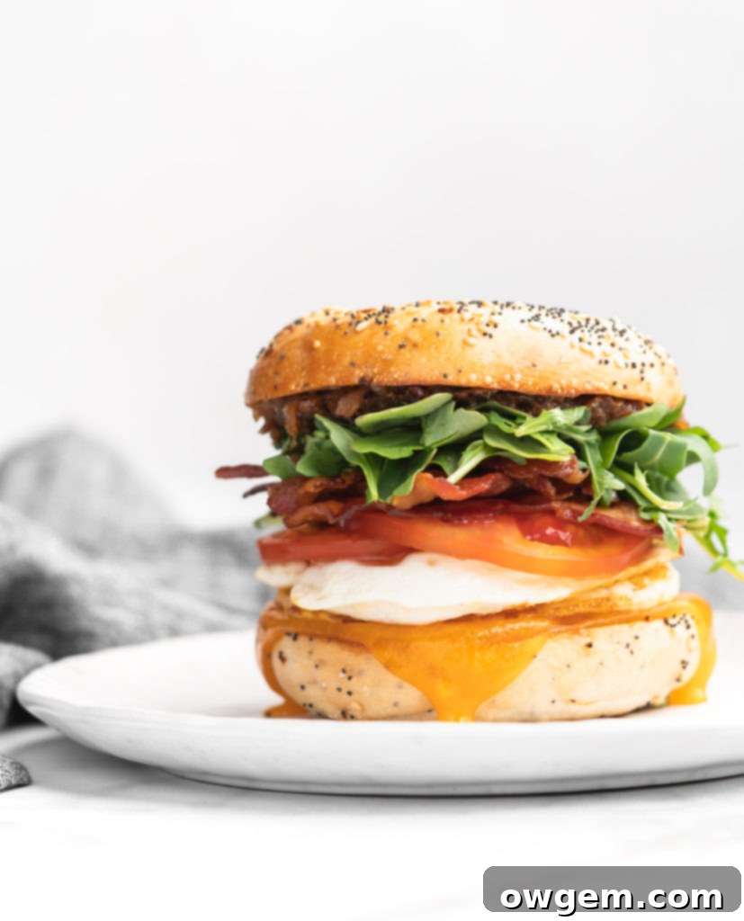 This bagel breakfast sandwich features cheddar, a fried egg, crispy bacon, juicy tomatoes, peppery arugula, sweet apple chutney, and savory bacon jam, all sandwiched between a garlicky everything bagel