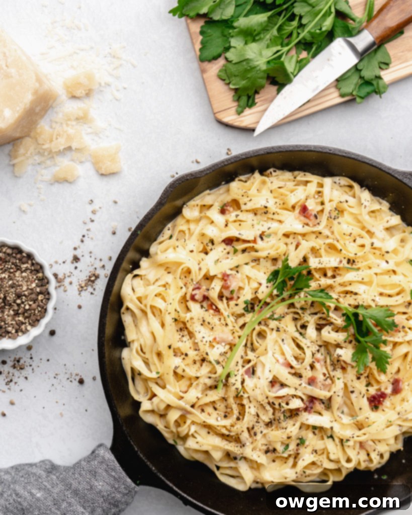 Creamy pasta carbonara is topped with fresh parsley and crispy pancetta in a pan, ready to be served