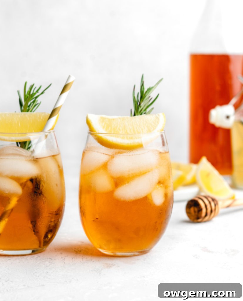 Two glasses of non-alcoholic Honey Rosemary Iced Tea on a wooden table, featuring rosemary and lemon garnish.