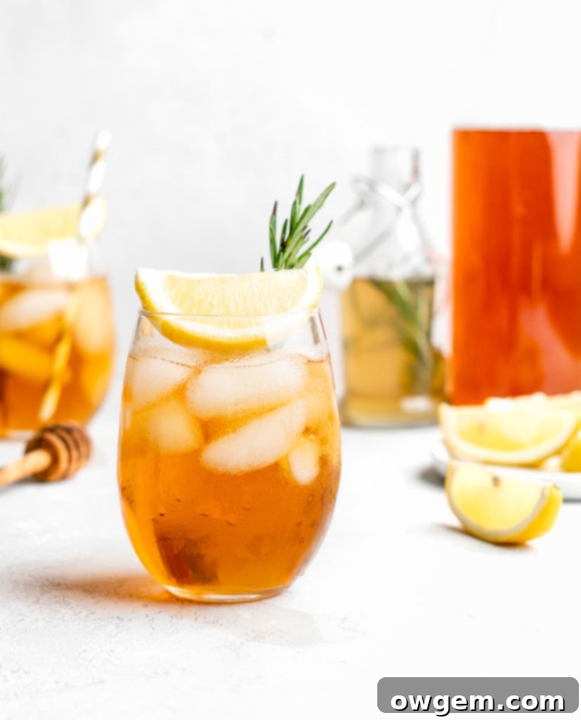A close-up of the Honey Rosemary Iced Tea drink, showing ice cubes, a lemon slice, and rosemary sprigs.