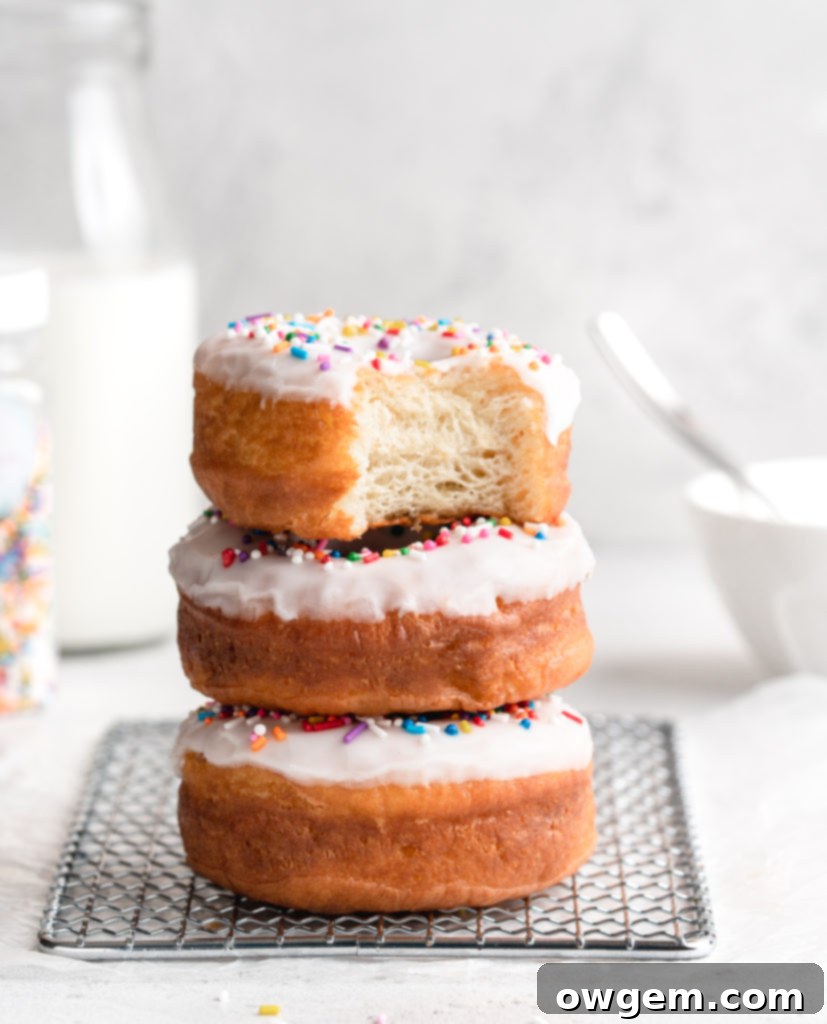Homemade brown butter and vanilla yeast donuts, generously frosted with a sweet white glaze and colorful rainbow sprinkles, resting on a cooling rack.
