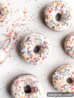 Perfectly cut, golden brown butter and vanilla donuts, frosted with a pristine white glaze and colorful rainbow sprinkles.