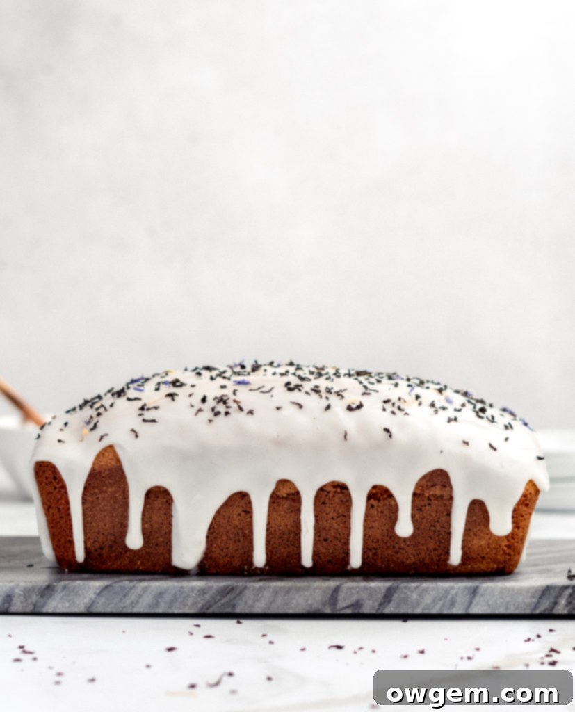 A close-up of a glazed Earl Grey Loaf Cake, showing the thick, opaque lemon honey glaze cascading down the sides.