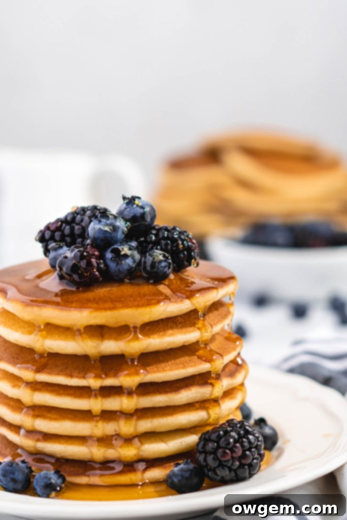 Fluffy Golden Buttermilk Pancakes stacked high, topped with fresh berries and drizzled with sweet maple syrup