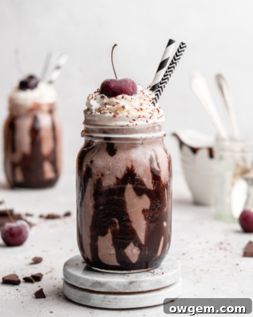 Two glasses of creamy Black Forest Chocolate Cherry Milkshakes, each topped with whipped cream and a cherry, showcasing the rich chocolate color and cherry accents.