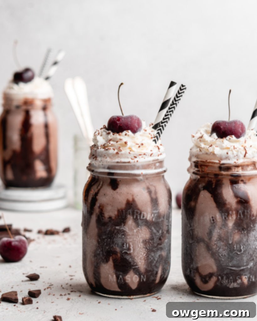 A Black Forest Chocolate Cherry Milkshake in a classic mason jar, beautifully topped with a swirl of whipped cream, a maraschino cherry, and a drizzle of chocolate syrup on the glass.