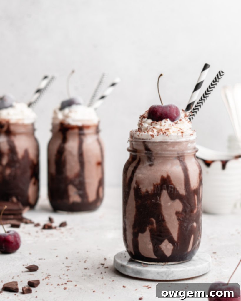 A single Black Forest Chocolate Cherry Milkshake, beautifully presented in a glass with a tall swirl of whipped cream, a cherry, and chocolate syrup drizzled inside the glass, ready to be enjoyed.