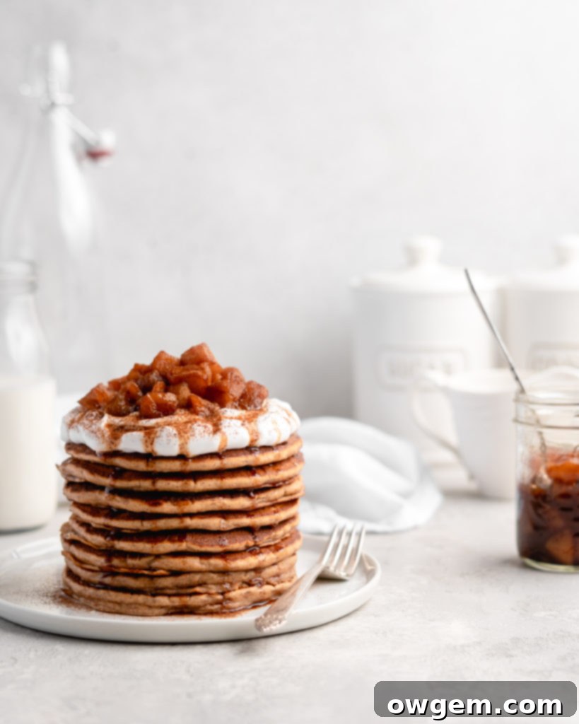 A stack of golden brown apple cinnamon pancakes drizzled with syrup and ready to be served
