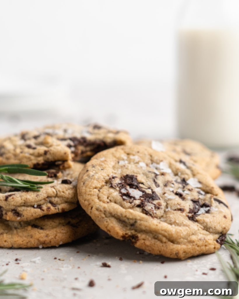 A stack of golden brown Rosemary Chocolate Chunk Cookies with visible melted chocolate and a hint of green rosemary.