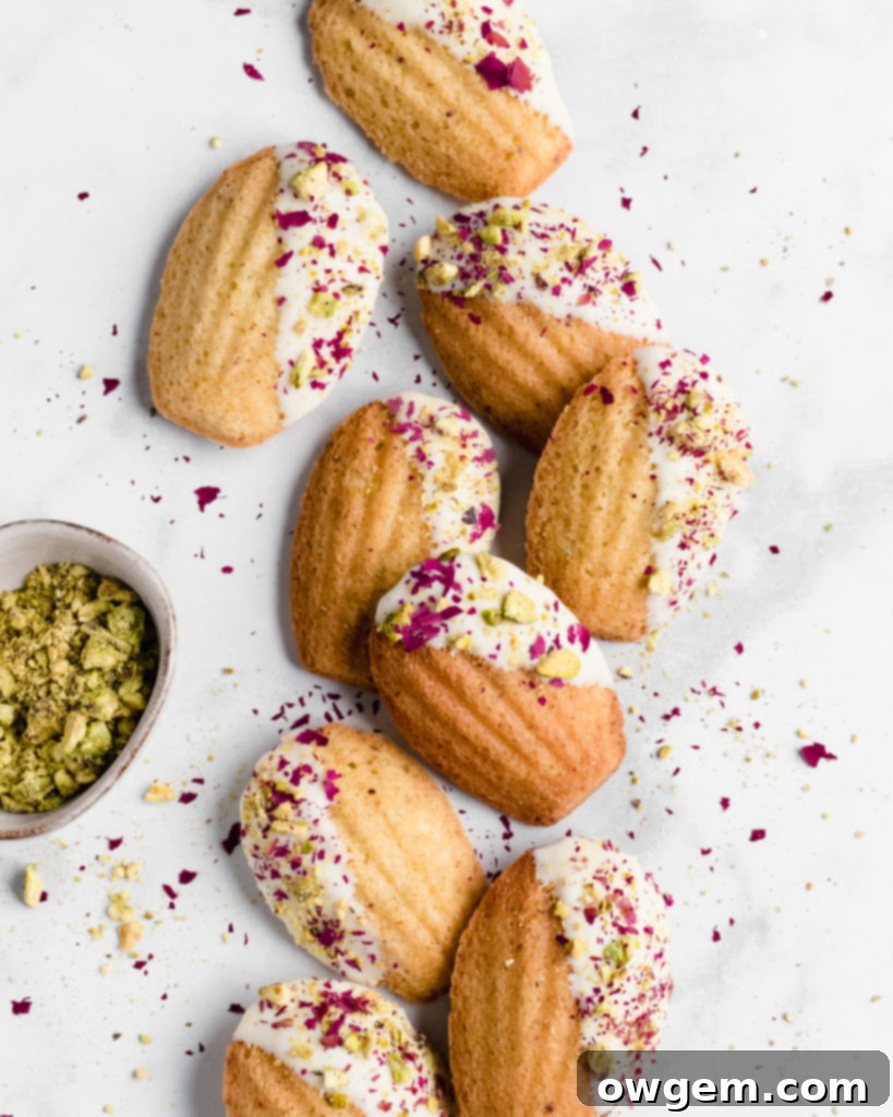Delicate Pistachio Rosewater Madeleines dipped in white chocolate and garnished with crushed pistachios.