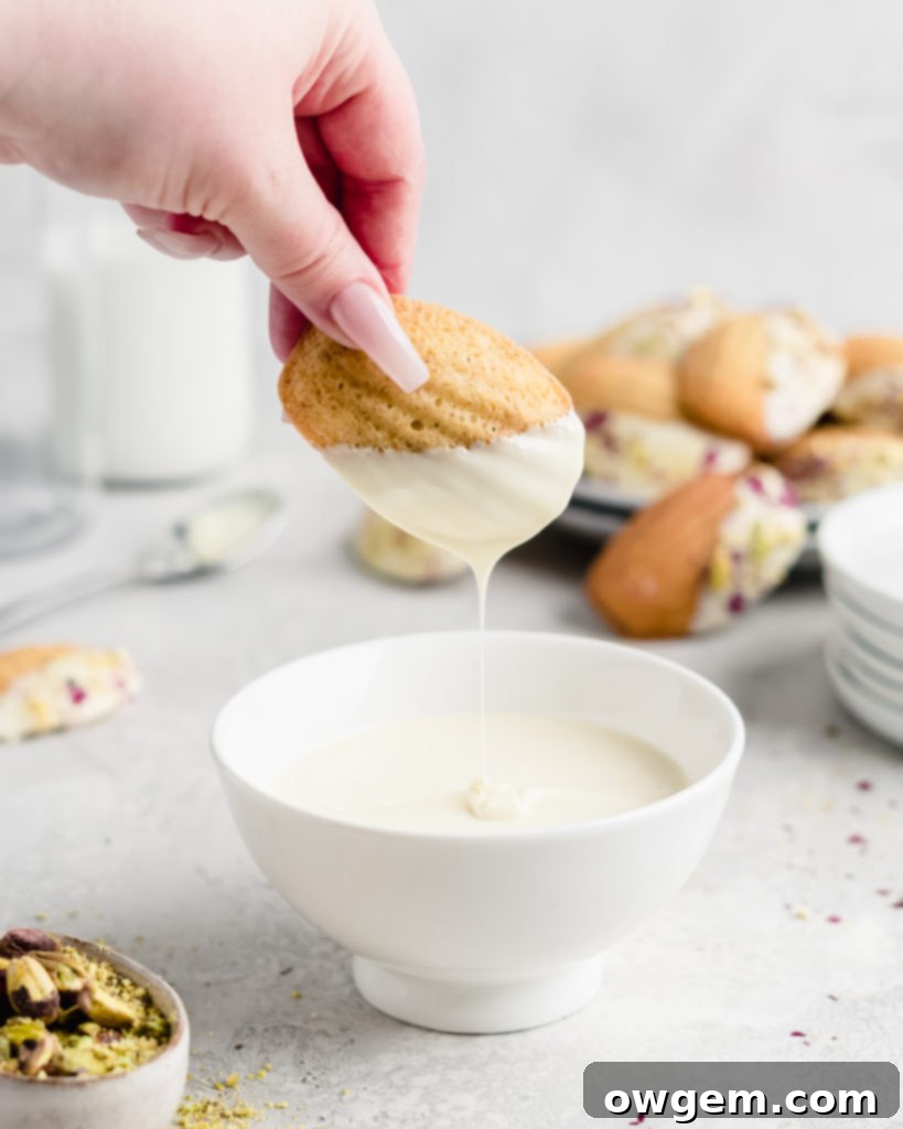 A close-up of a finished Pistachio Rosewater Madeleine with white chocolate and crushed pistachios.
