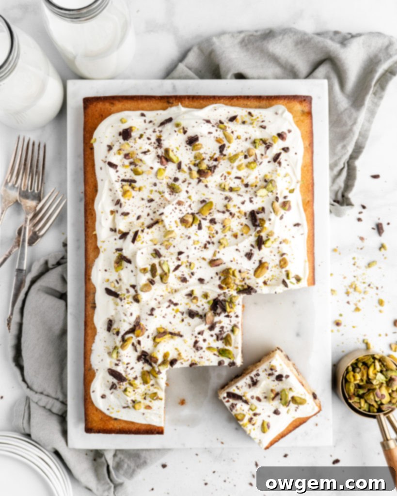 A close-up shot of the finished Cannoli Cake, highlighting the creamy texture of the whipped ricotta frosting adorned with chocolate and pistachios.