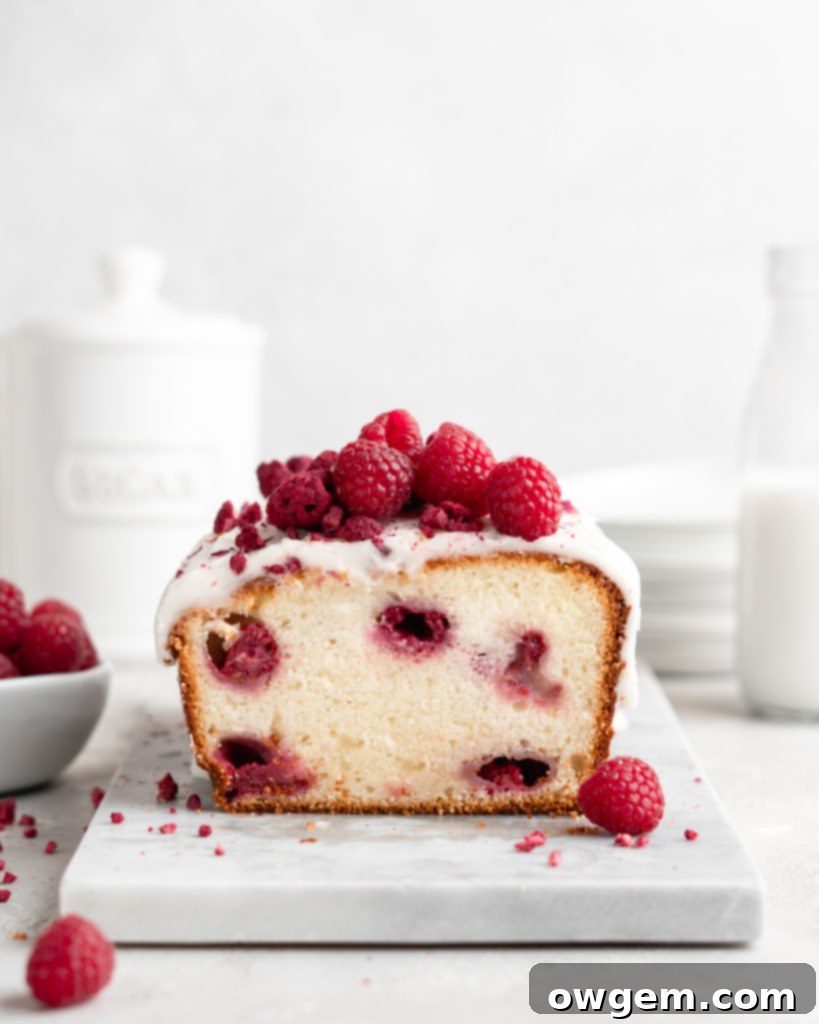 Close-up of a slice of Raspberry Rose Yogurt Loaf Cake, showing the moist crumb, juicy raspberries, and a generous coating of rosewater glaze.