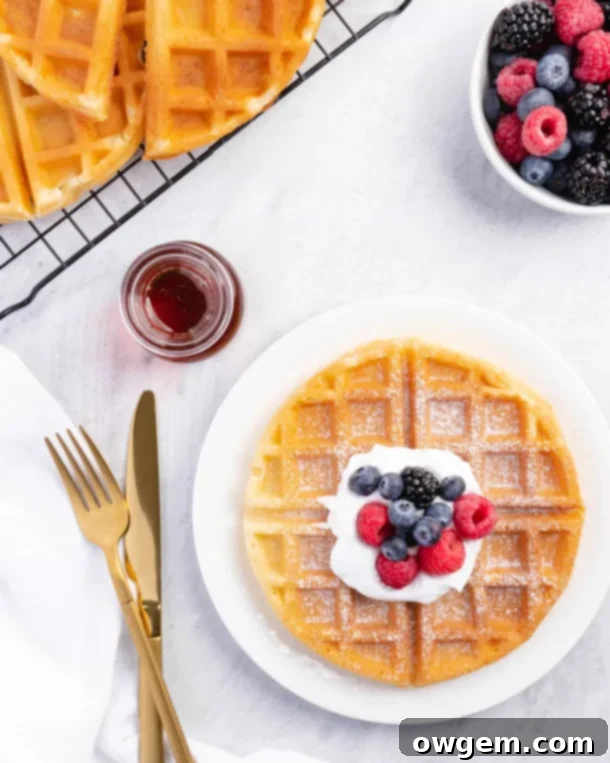 A bowl of glossy, stiff meringue with a whisk, ready to be folded into waffle batter