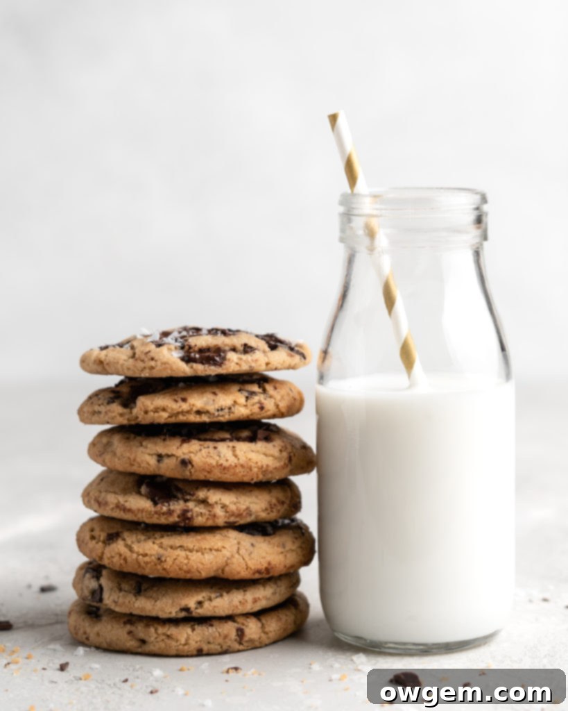 Two hands reaching for a freshly baked chewy brown butter chocolate chip cookie, demonstrating its allure.