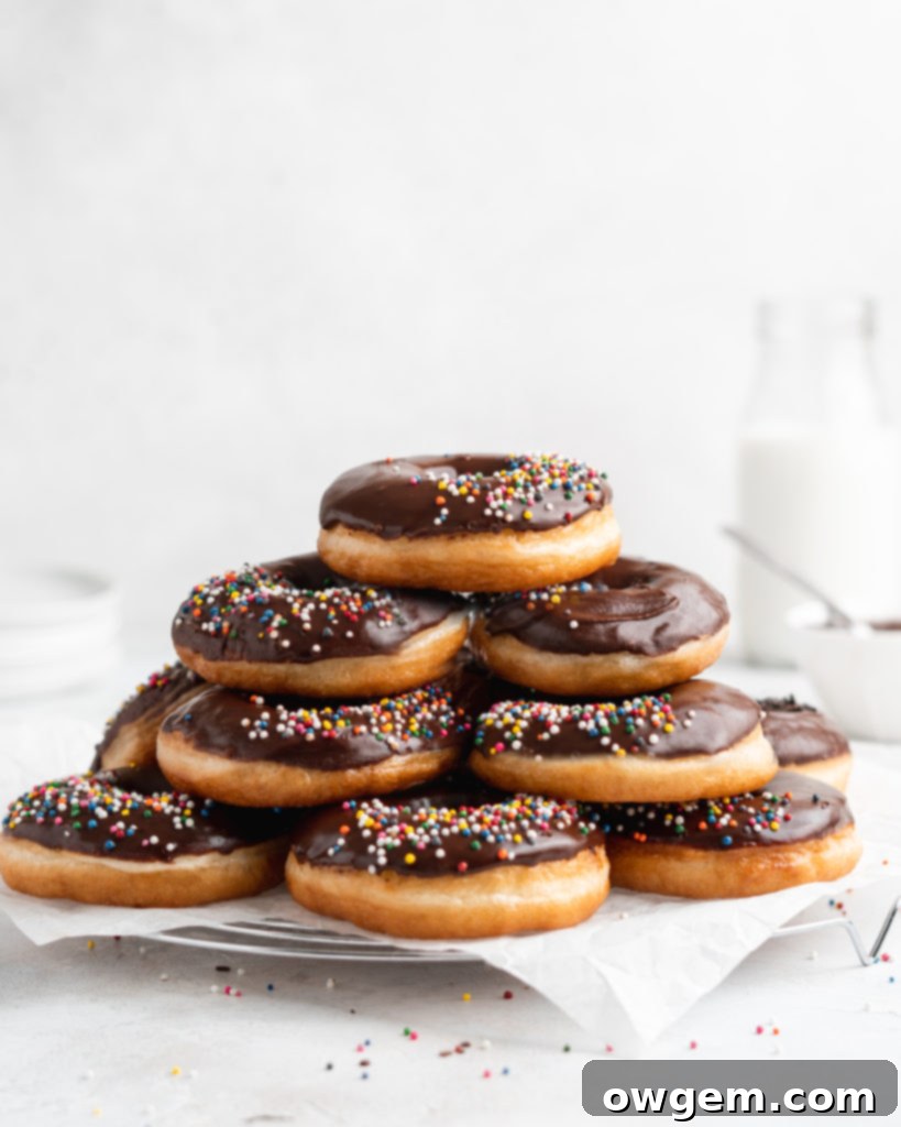 Fluffy golden fried yeast donuts are glazed with a shiny chocolate glaze and colorful round sprinkles
