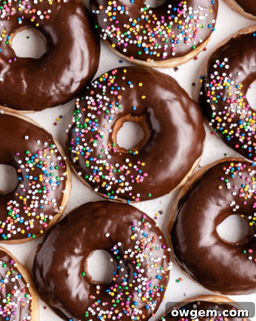 Fluffy golden fried yeast donuts are glazed with a shiny chocolate glaze and colorful round sprinkles