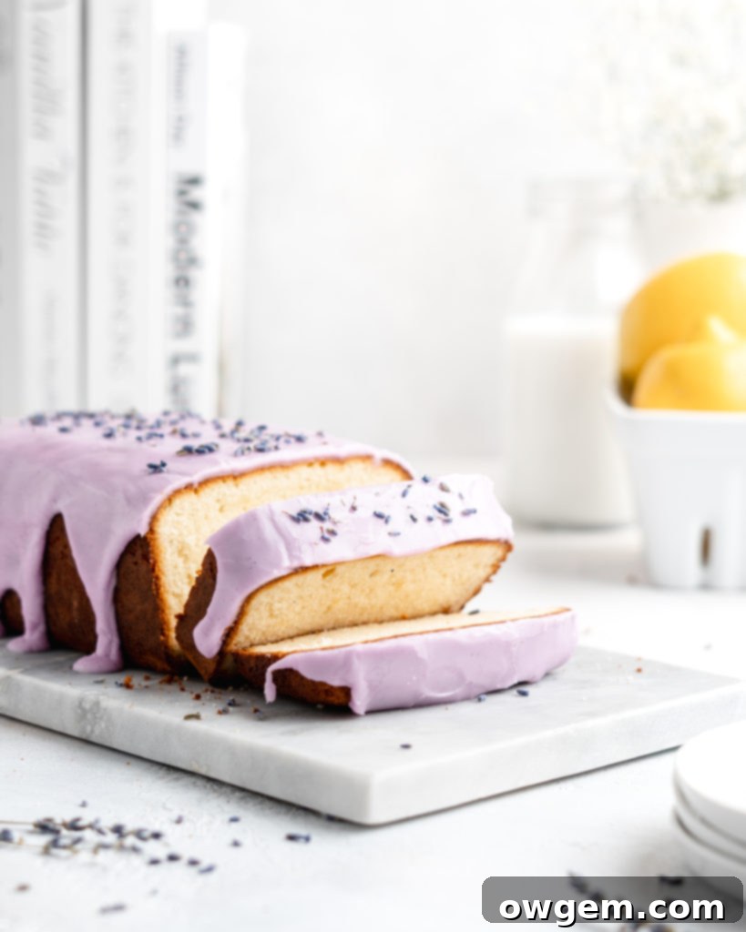 Fluffy and moist Lemon and lavender loaf cake is glazed in a purple coloured vanilla glaze, resting on a rustic wooden board