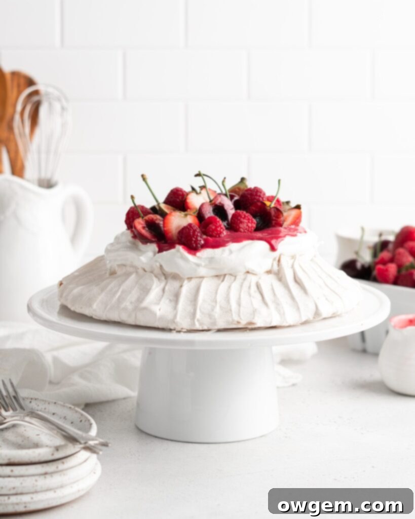 A stunning Summer Berry Pavlova topped with fresh raspberries, blueberries, strawberries, and a swirl of raspberry curd and whipped cream, ready to be served.