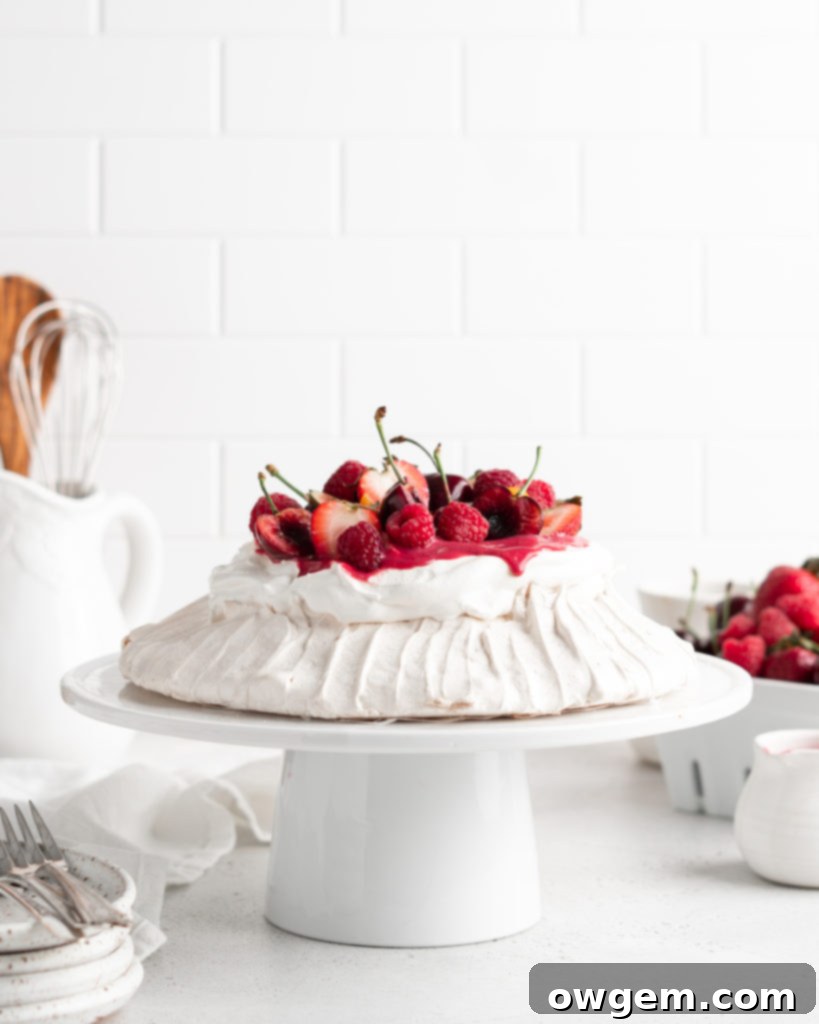 A beautifully decorated Summer Berry Pavlova, showcasing its various layers of meringue, whipped cream, raspberry curd, and mixed berries.
