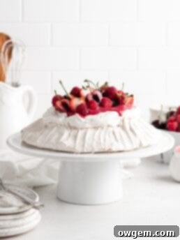 Fluffy and delicious Pavlova is topped with vibrant raspberry curd, fresh whipped cream, and an abundance of mixed summer berries.