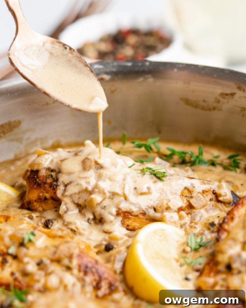 Chicken in pan, topped with white wine cream sauce, spoon drizzling sauce over top