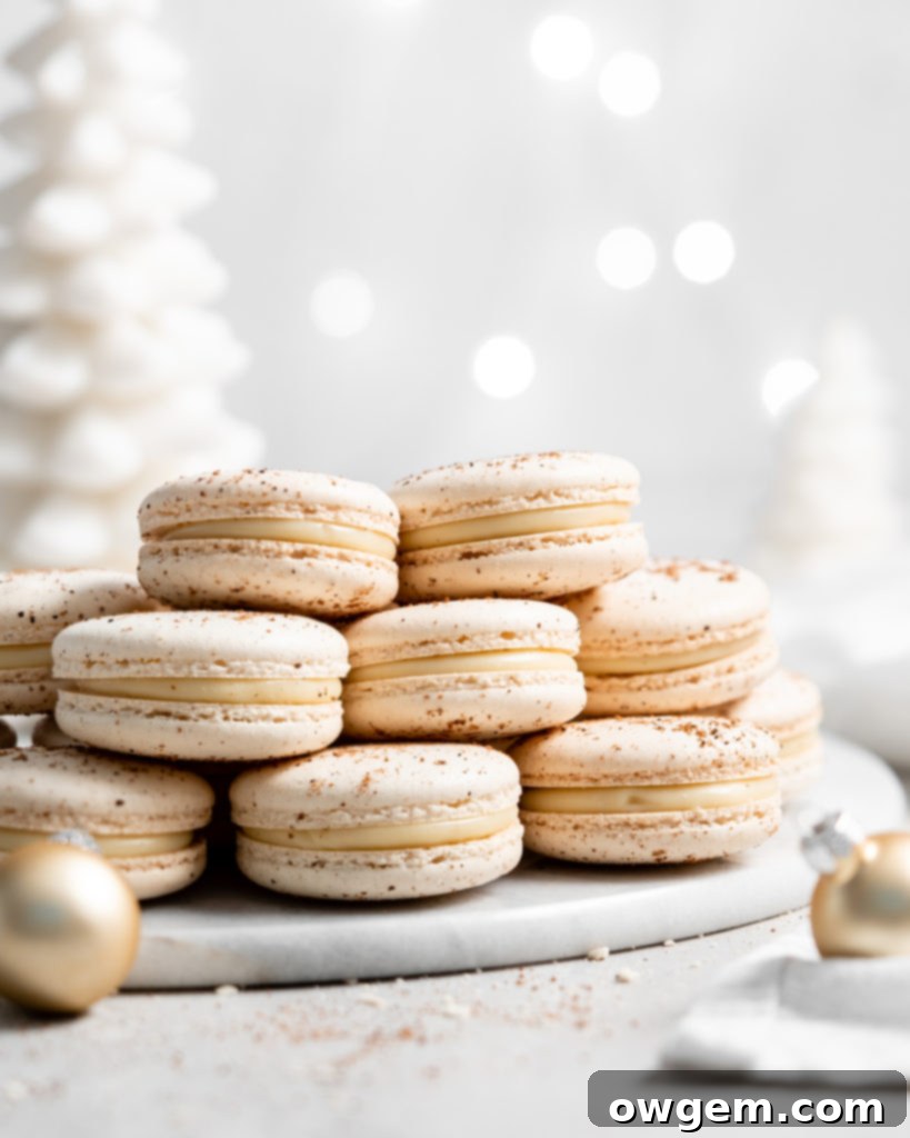 Close-up of three finished eggnog macarons, highlighting their 'feet' and creamy filling, arranged on a rustic wooden surface.