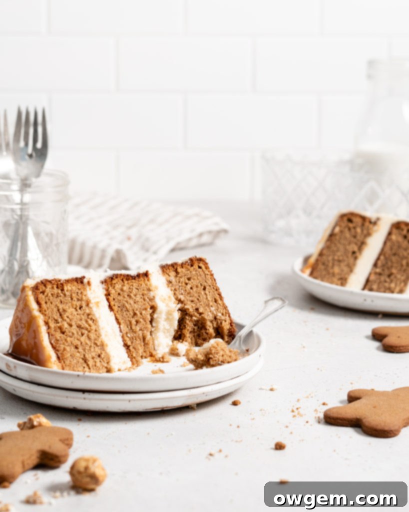A festive gingerbread layer cake on a stand, decorated with cream cheese frosting, salted caramel, and gingerbread men cookies