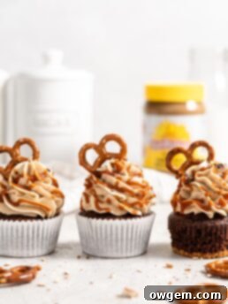 SunButter Pretzel Chocolate Cupcakes topped with a beautiful swirl of SunButter frosting, adorned with mini pretzels, and a luscious caramel drizzle.