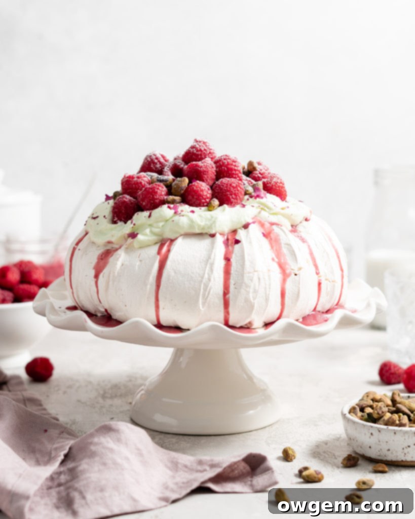 Thick fluffy pavlova topped with whipped pistachio white chocolate ganache and fresh raspberry curd