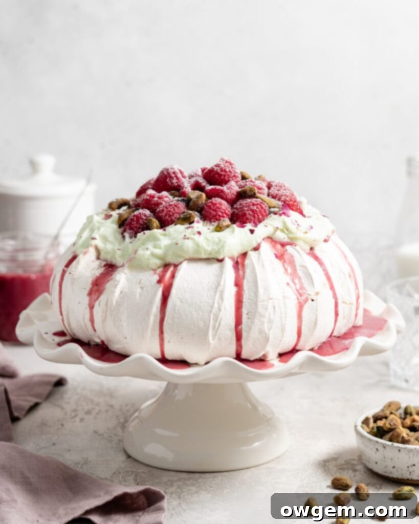 Thick fluffy pavlova topped with whipped pistachio white chocolate ganache and fresh raspberry curd