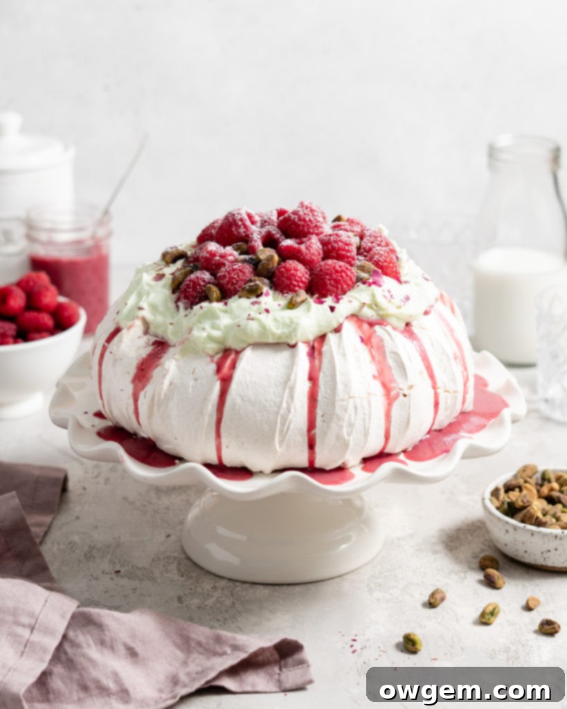Thick fluffy pavlova topped with whipped pistachio white chocolate ganache and fresh raspberry curd
