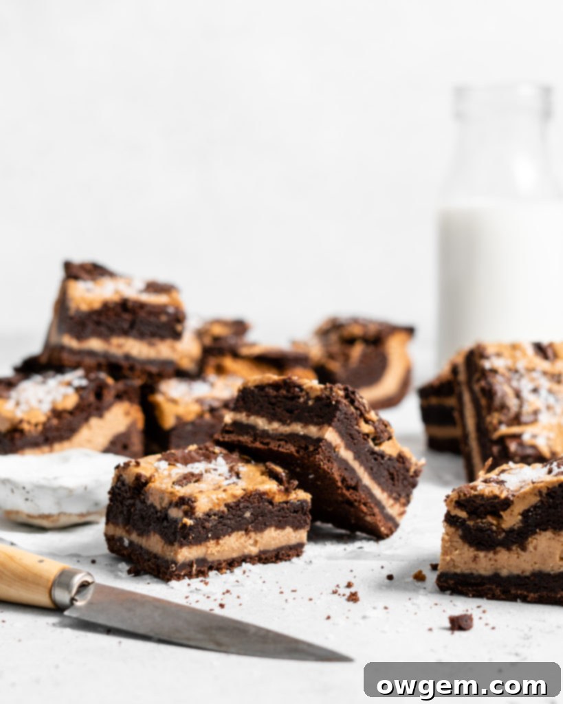 Raw brownie batter in a baking pan, topped with a layer of creamy peanut butter and ready for the final brownie batter layer.