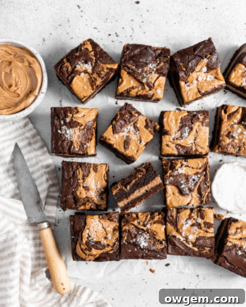 Unbaked brownie batter in a square pan with peanut butter dollops swirled on top, ready for the oven.