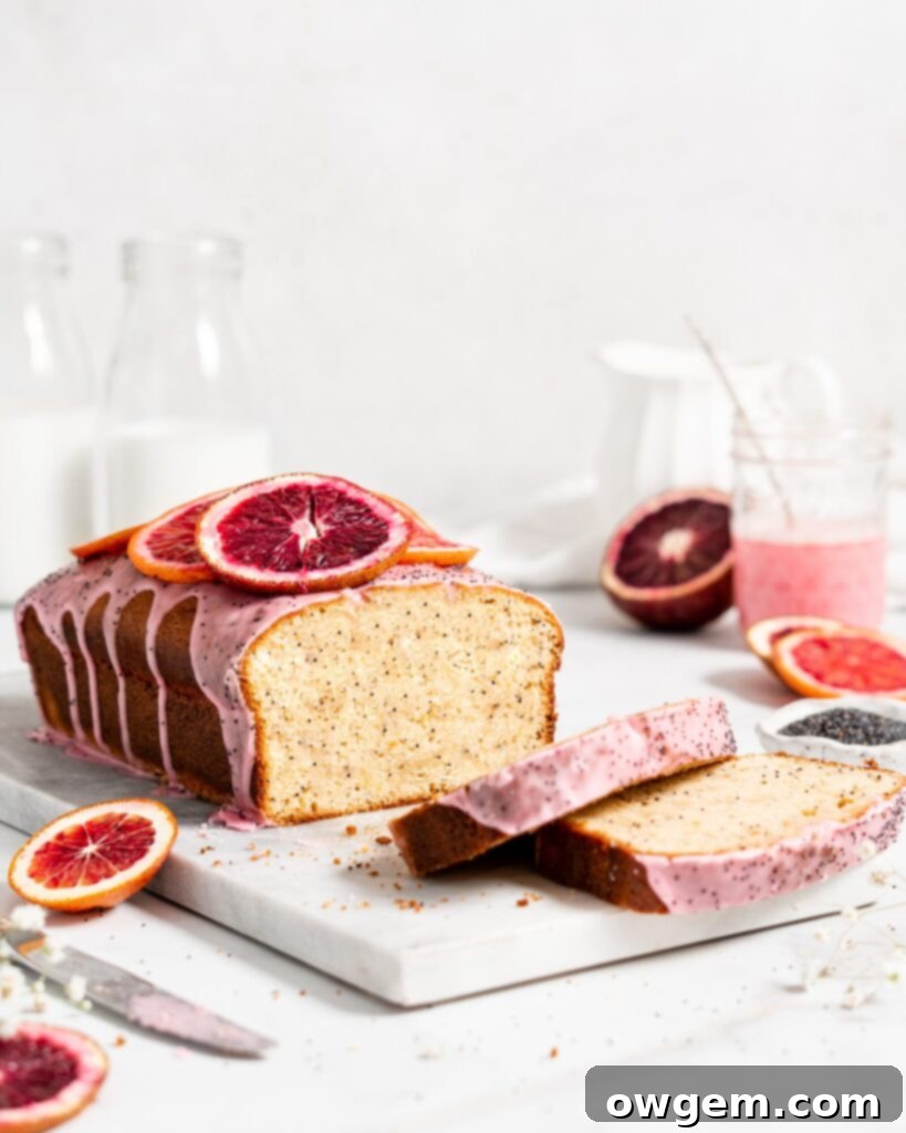 A beautifully sliced Blood Orange Poppy Seed Loaf with a vibrant blood orange glaze, garnished with poppy seeds, resting on a white platter.