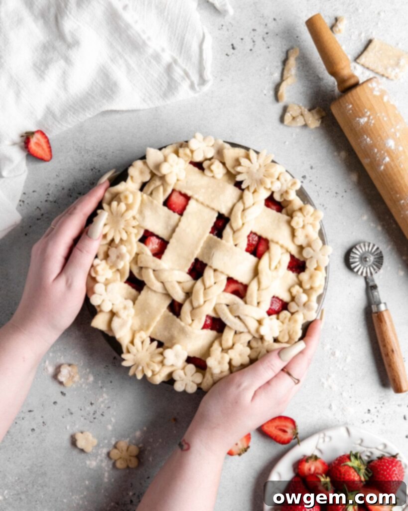 Classic strawberry pie with a golden, flaky pie crust and a rich, thick strawberry filling, garnished with fresh strawberries on a rustic wooden surface.