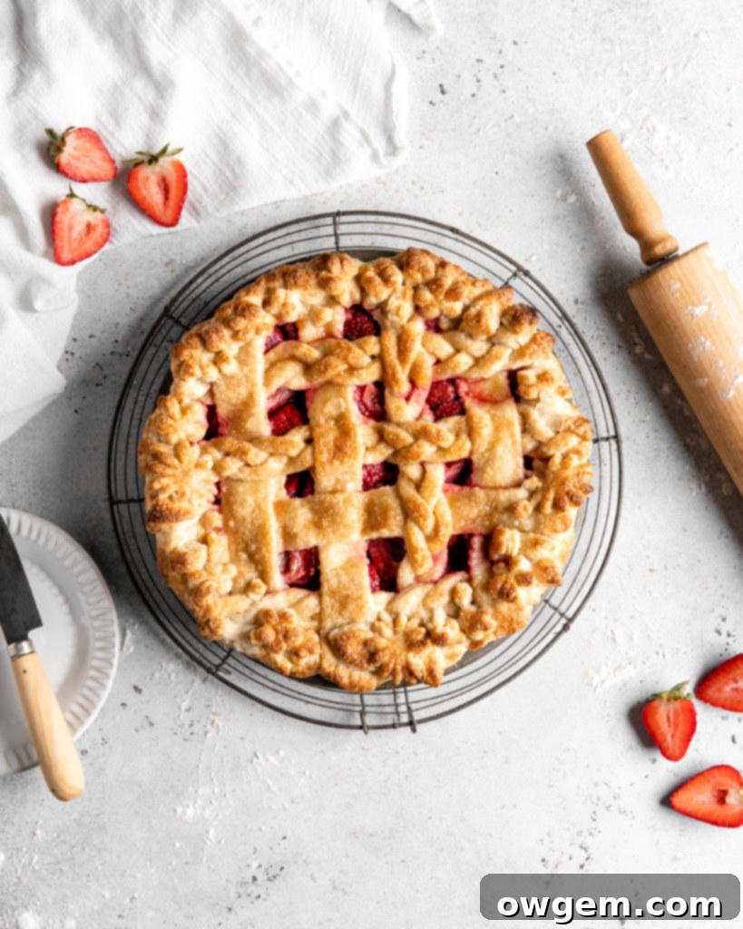 Close-up of a rustic strawberry pie with a perfectly flaky pie crust, featuring a thick, jammy strawberry filling peeking through a lattice top.