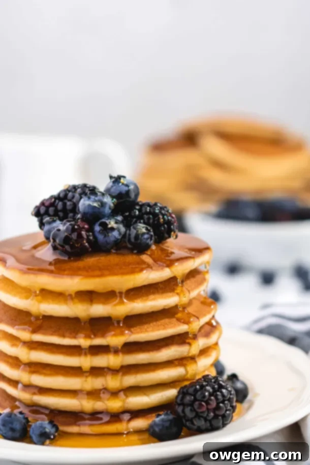 Fluffy Golden Buttermilk Pancakes stacked high, topped with fresh berries and drizzled with sweet maple syrup