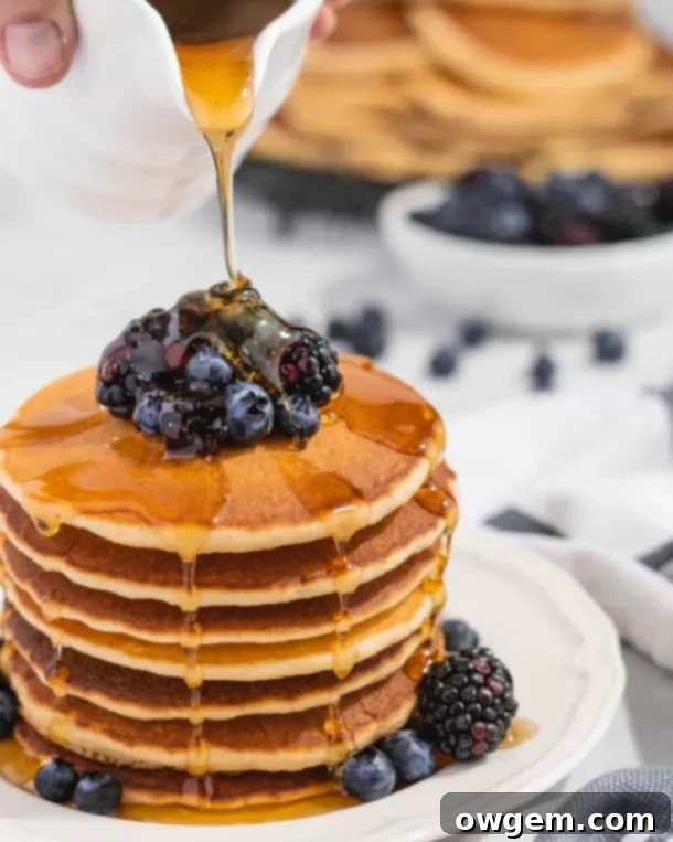 Fluffy Golden Buttermilk Pancakes stacked high, topped with fresh berries and drizzled with sweet maple syrup