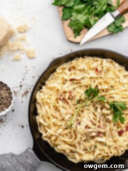 Creamy pasta carbonara is topped with fresh parsley and crispy pancetta in a pan, ready to be served