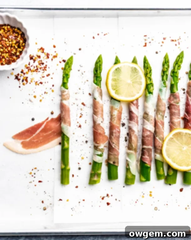 Prosciutto wrapped around fresh green asparagus, topped with lemons, ready to be baked
