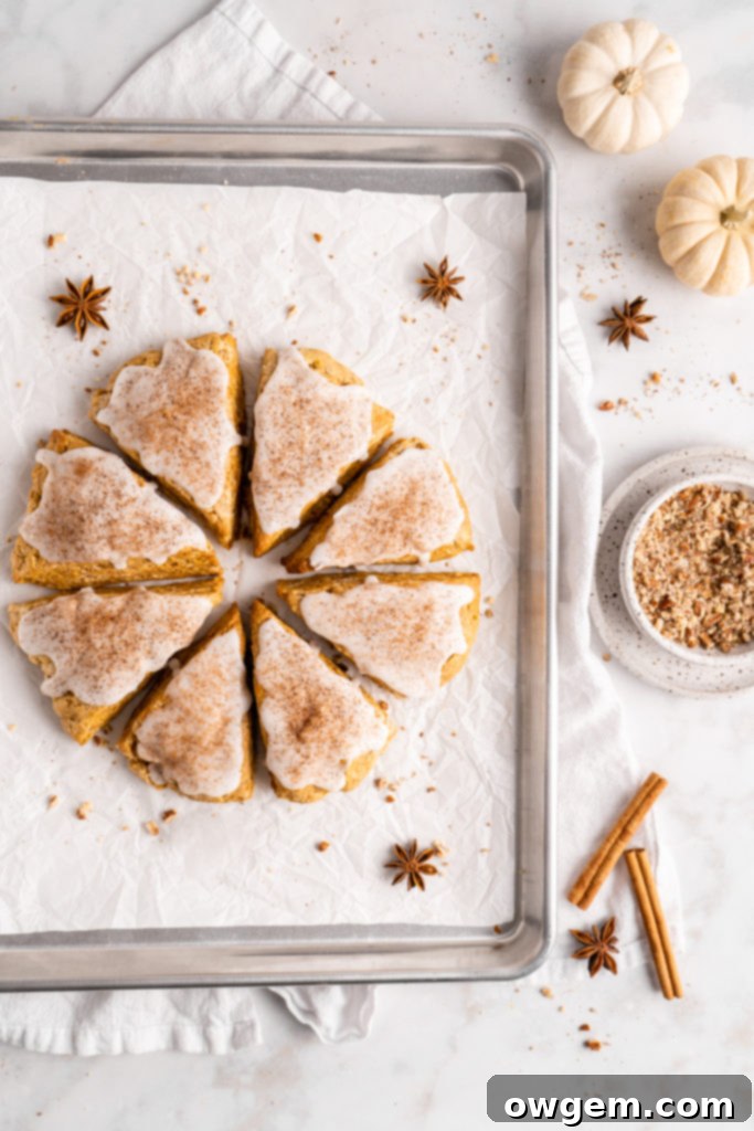 flaky and tender chai pumpkin scones with vanilla glaze, sprinkled with cinnamon and cloves