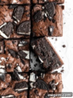 Crinkly top brownies with Oreos on top, one brownie turned on its side, showcasing its fudgy layers.