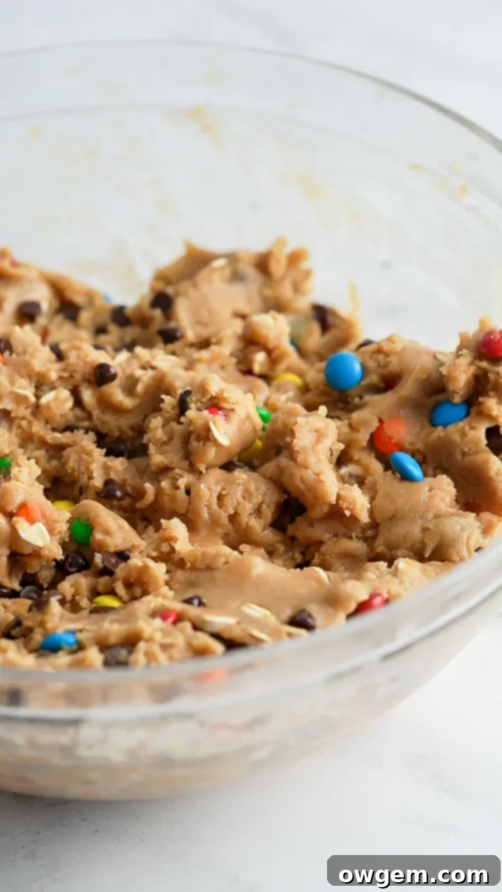 A large mixing bowl filled with peanut-free monster cookie dough, studded with colorful M&M's and chocolate chips, ready for scooping.