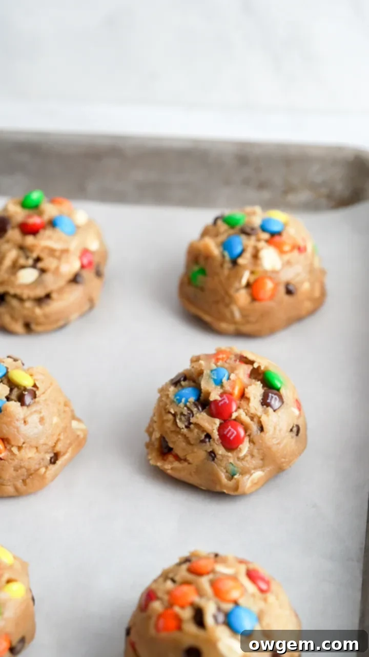 Perfectly portioned scoops of monster cookie dough on a parchment-lined baking sheet before baking.