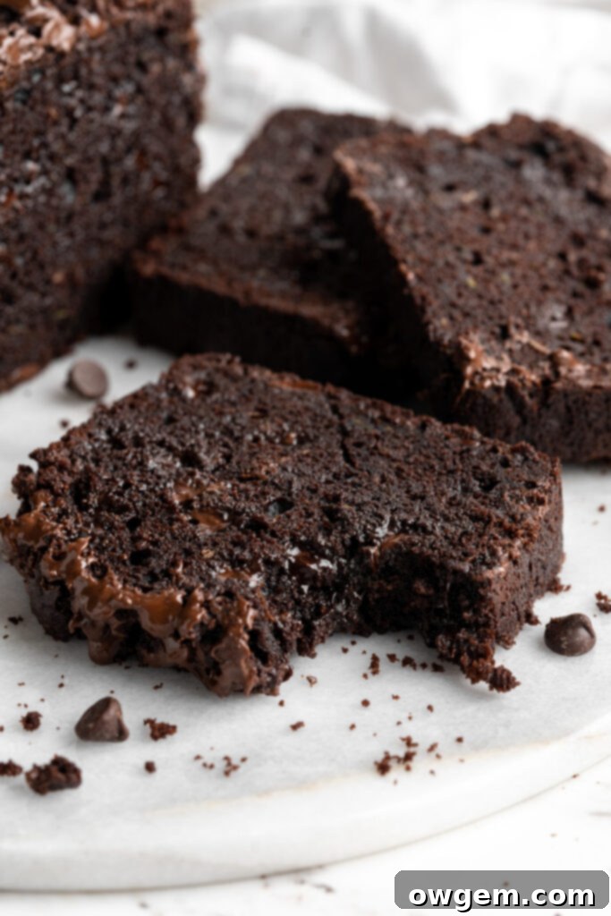 Slices of rich triple chocolate zucchini bread on a cutting board, showcasing its fudgy texture and melted chocolate chips.