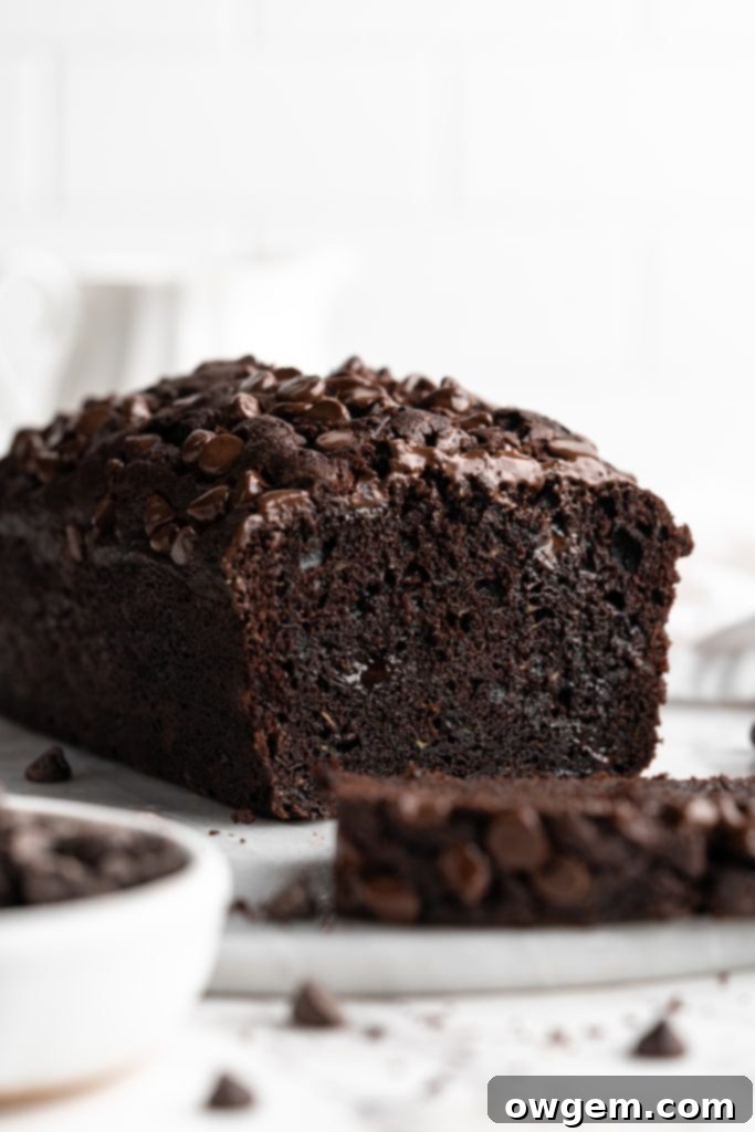A beautifully baked triple chocolate zucchini loaf cake on a white serving plate, with a few slices already cut and visible.